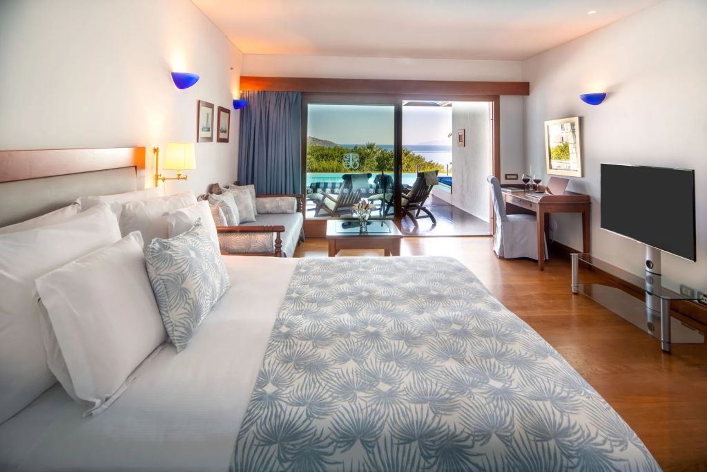 Helles Zimmer mit Doppelbett und Sofaecke sowie Zugang zu Terrasse mit Meerblick.