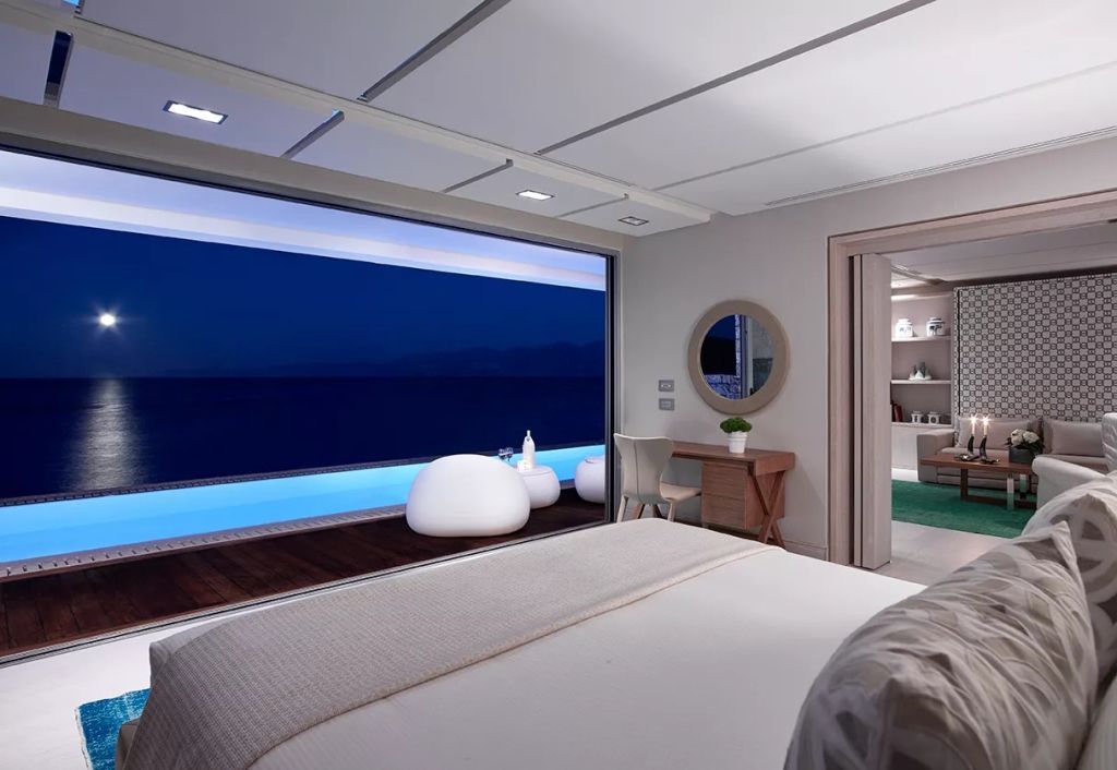 Schlafzimmer bei Nacht mit Blick auf den beleuchteten Privatpool im Elounda Beach Hotel