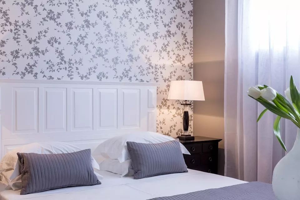 Doppelbett in elegantem Interieur mit floralem Tapetenmuster.