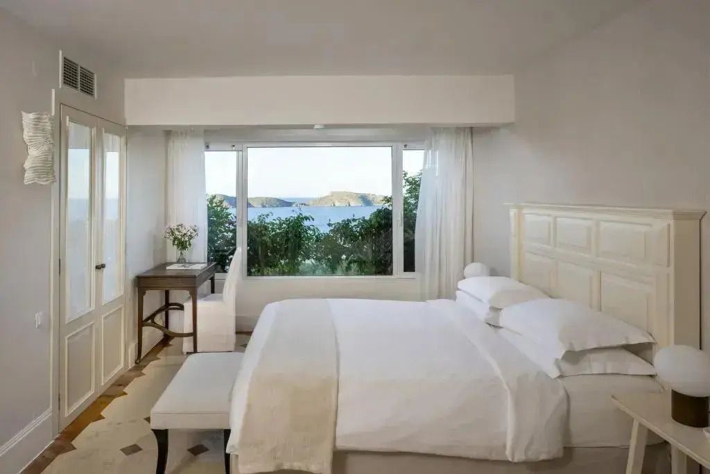 Helles Schlafzimmer mit großem Fenster und Meerblick. Doppelbett und Schreibtisch.