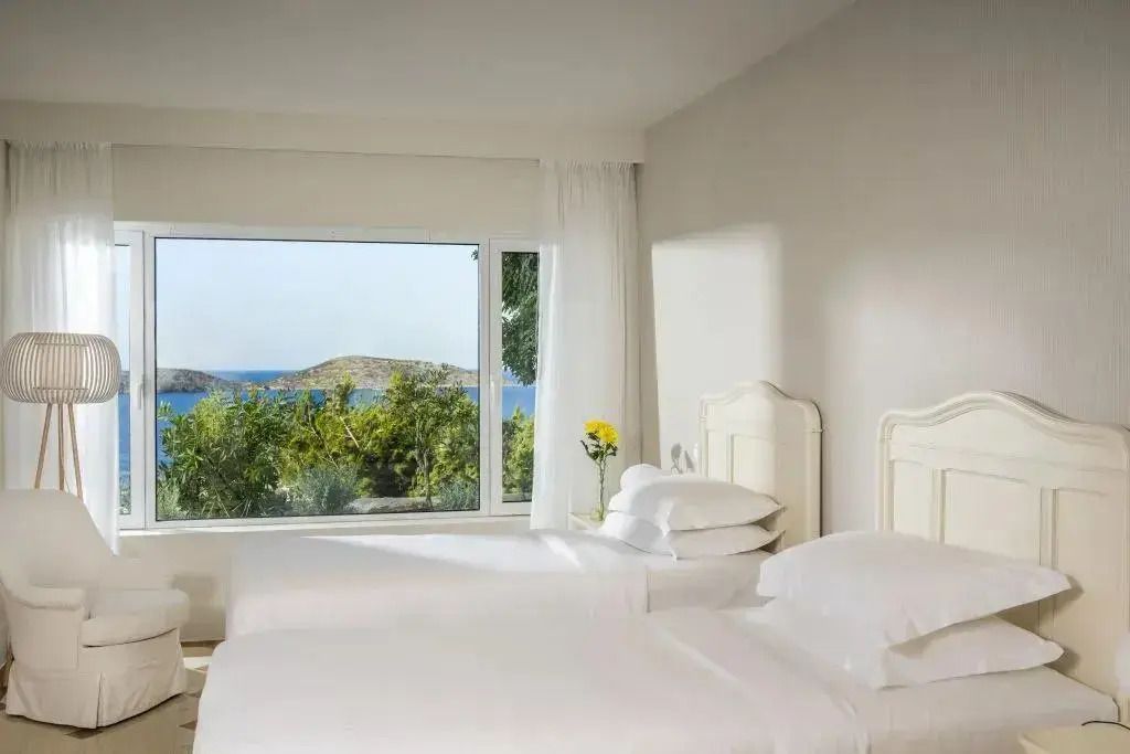 Zweibettzimmer mit Meerblick durch ein großes Fenster. Frische Blumen auf dem Tisch.