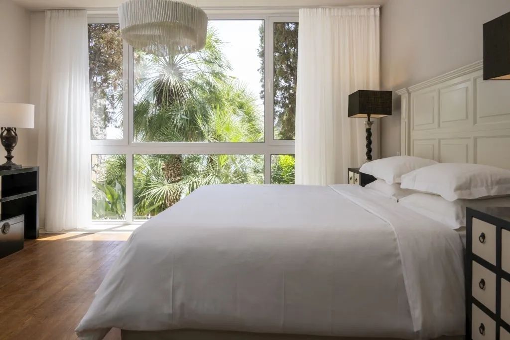Elegantes Schlafzimmer mit Blick auf Palmen durch große Fenster