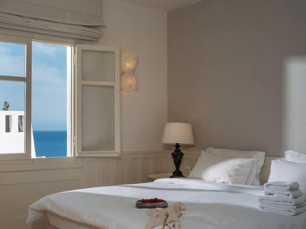Helles Schlafzimmer mit Doppelbett und offenem Fenster mit Meerblick