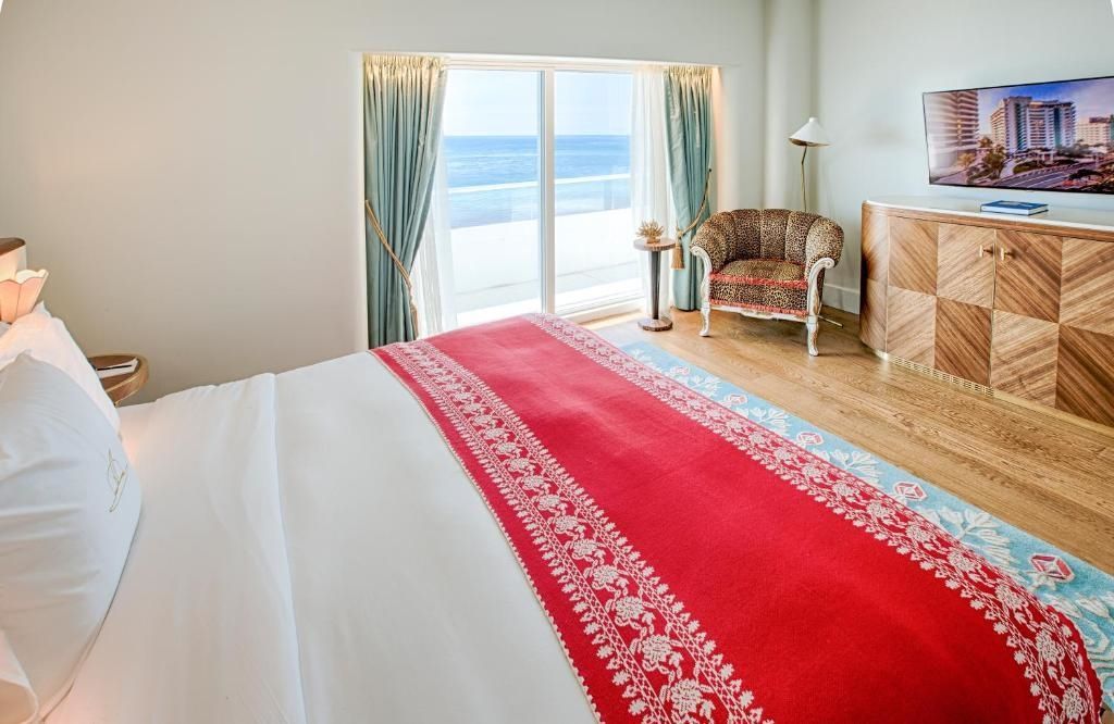 Komfortables Bett mit rotem Überwurf und Meerblick aus dem Fenster.
