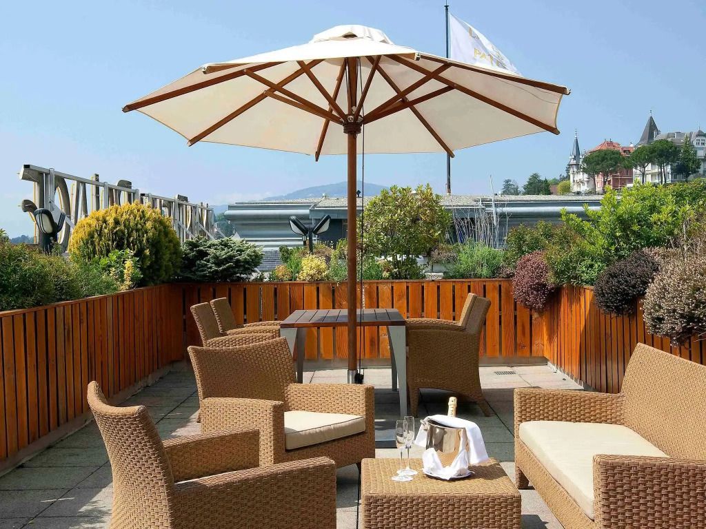 Terrasse mit gemütlichen Rattanmöbeln und Sonnenschirm Blick auf Montreux