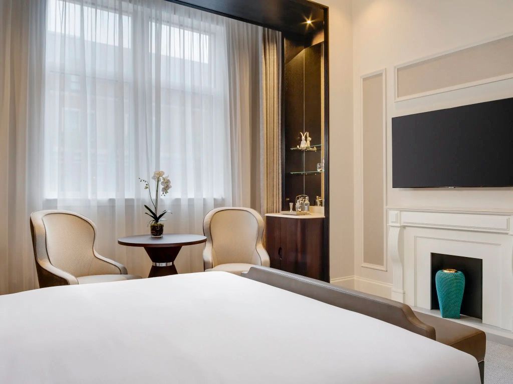 Helles Hotelzimmer mit zwei Sesseln, Tisch und Kamin. Modern und elegant eingerichtet.