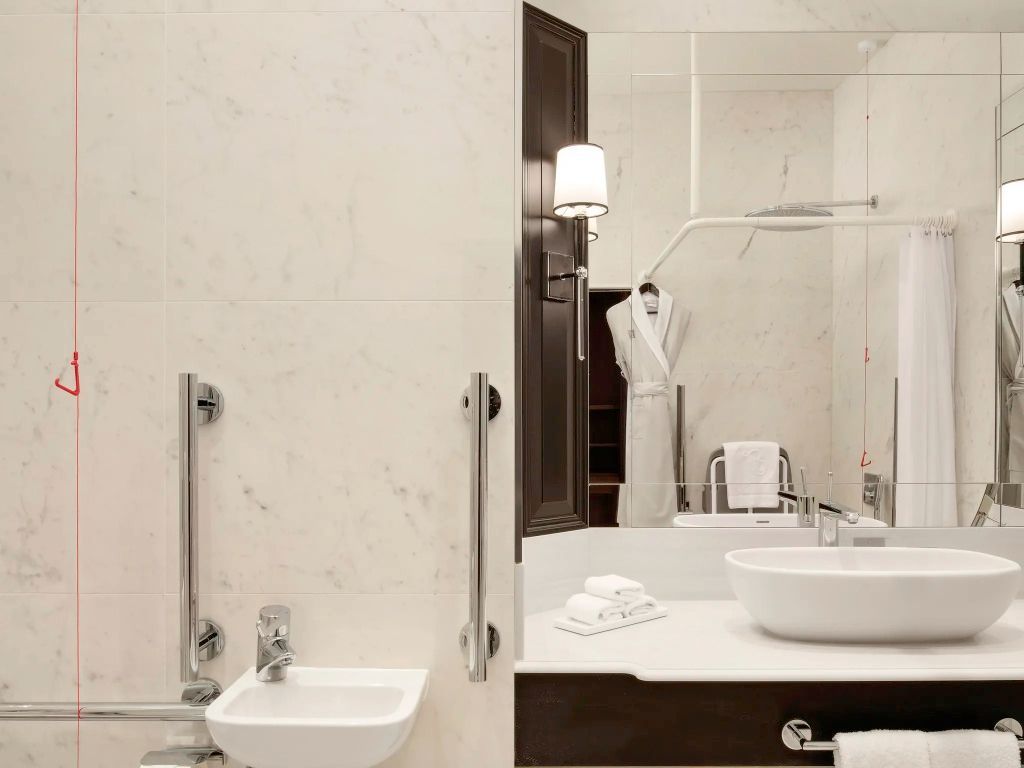 Modernes Badezimmer mit Haltegriffen, Waschbecken und großem Spiegel. Weißes Design.
