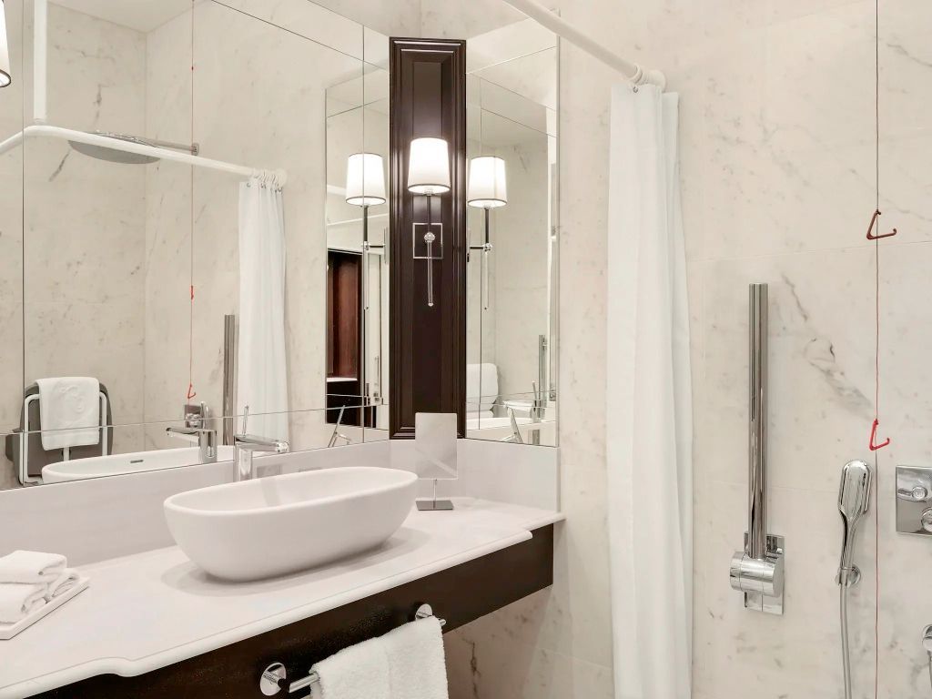 Badezimmer mit modernem Waschbecken, Haltegriffen und großen Spiegeln. Helle Ausstattung.