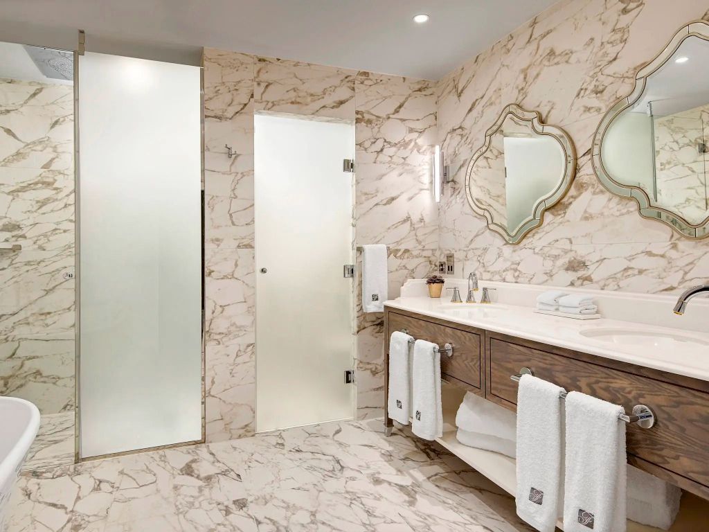 Luxuriöses Badezimmer in Marmoroptik mit Doppelwaschbecken und Glastür