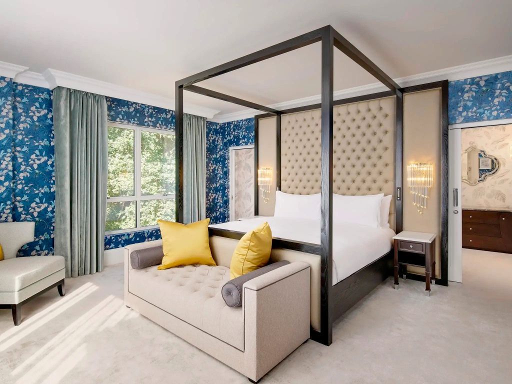 Luxuriöses Schlafzimmer mit Himmelbett, modernem Sofa und großen Fenstern mit Blick ins Grüne.