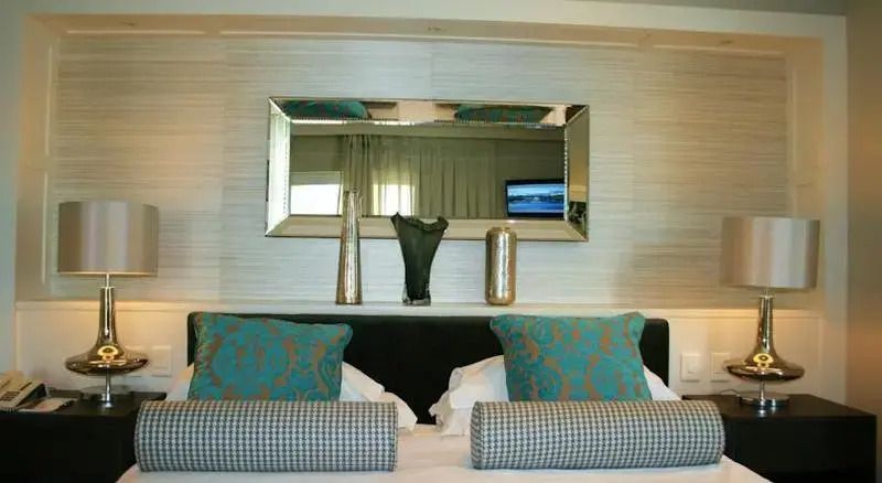 Luxuriöses Schlafzimmer mit dekorativen Kissen und Spiegel über dem Bettkopf