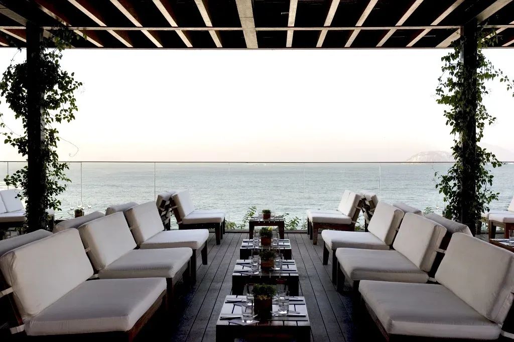 Terrasse mit weißen Sofas und Meerblick unter Holzdach mit grünem Bewuchs