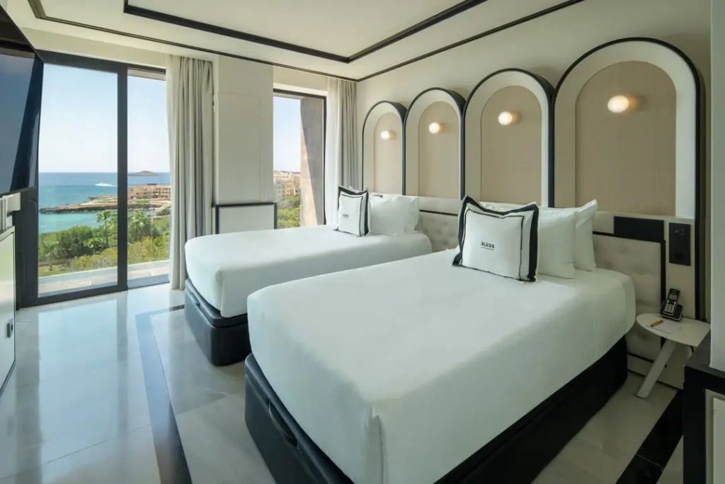 Helles Zimmer mit zwei Einzelbetten und Meerblick durch große Fenster.