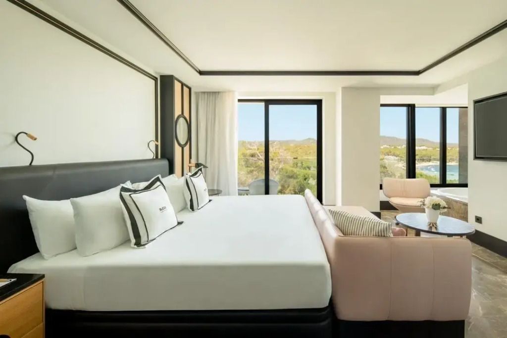 Lichtdurchflutetes Zimmer mit Doppelbett und Meerblick durch große Fenster