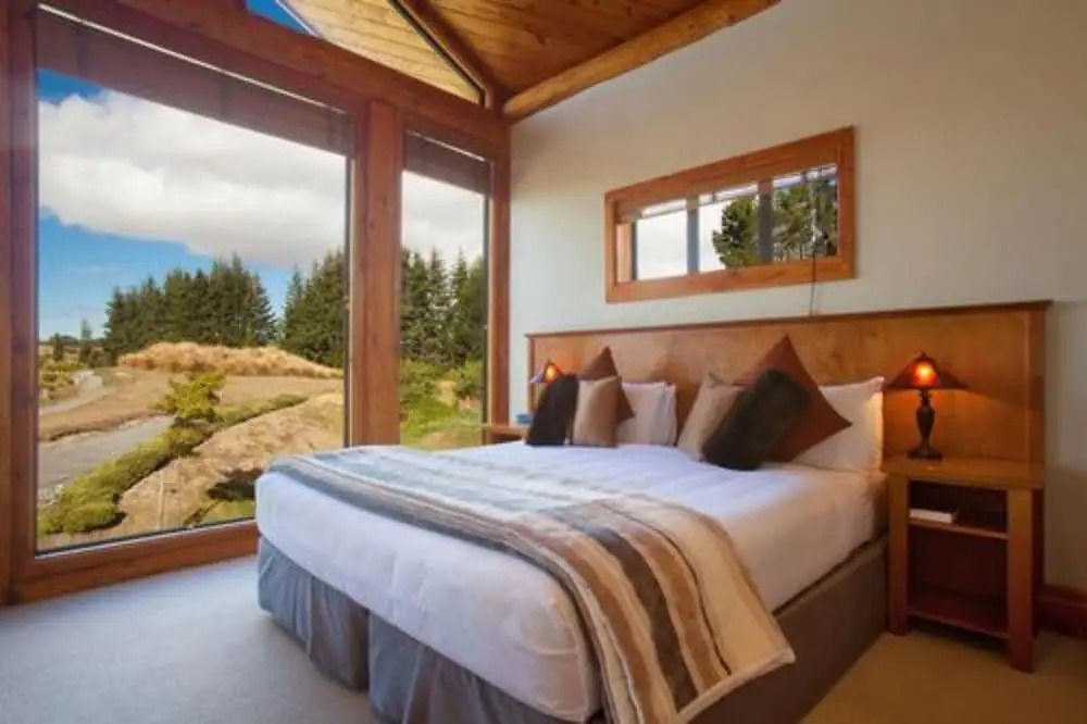 Schlafzimmer mit großem Bett, Holzakzenten und großen Fenstern.