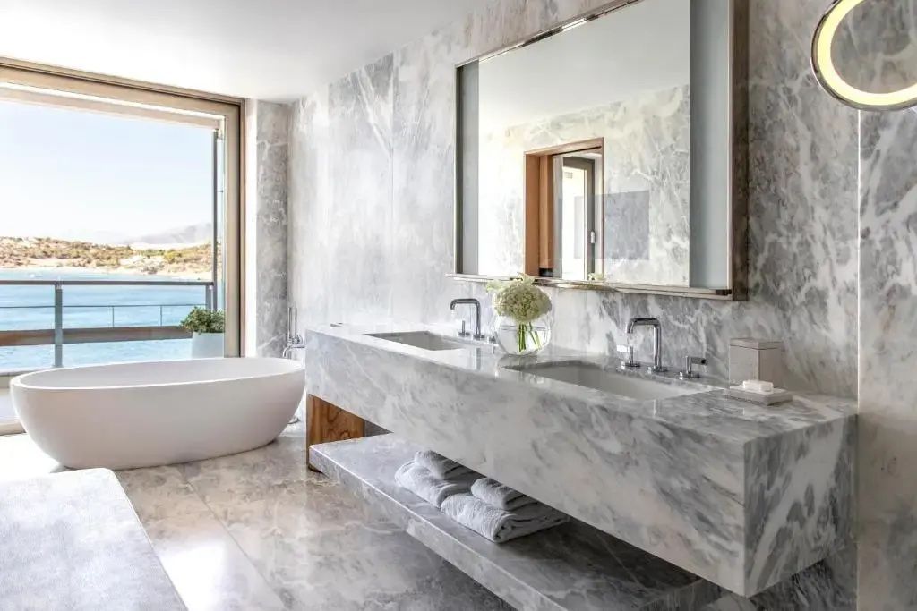 Eleganter Marmorwaschtisch und freistehende Badewanne mit Blick auf das Meer.