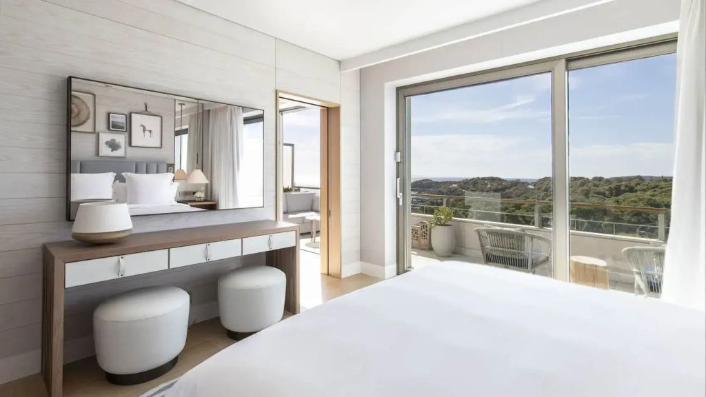 Hell eingerichtetes Schlafzimmer der Suite mit Schminktisch und Zugang zum Balkon.