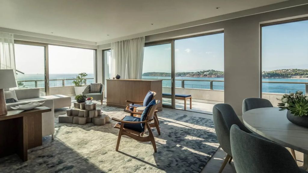 Großzügiger Wohnbereich mit Holzsesseln, Panoramafenstern und direktem Zugang zur Meerblick Terrasse.