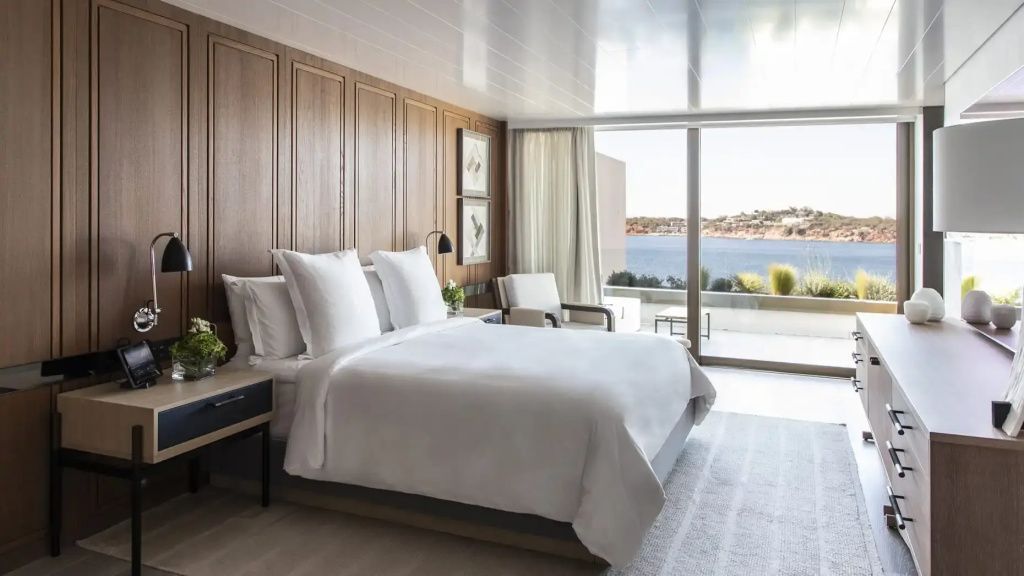 Schlafbereich der Nafsika Ambassador Suite mit Kingsize-Bett und Meerblick durch bodentiefe Fenster.