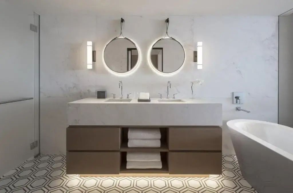 Marmorbadezimmer mit Doppelwaschbecken und zwei kreisförmigen, beleuchteten Spiegeln.