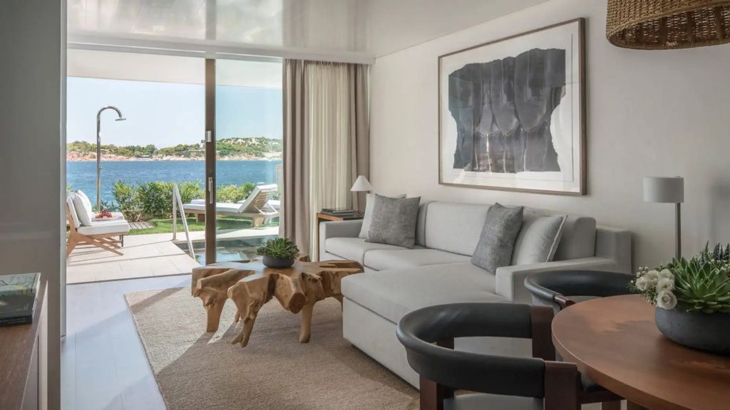 Wohnbereich der Suite mit modernem Sofa, Holztisch und Panoramablick auf das Meer.