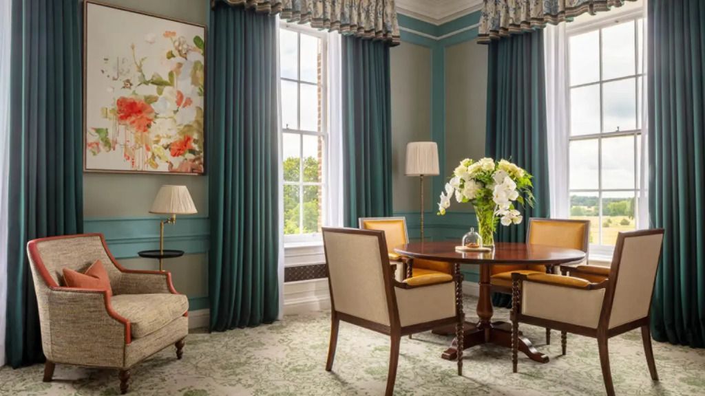 Eleganter Wohnbereich mit großem Fenster, Tisch, Stühlen und Blumenarrangement.
