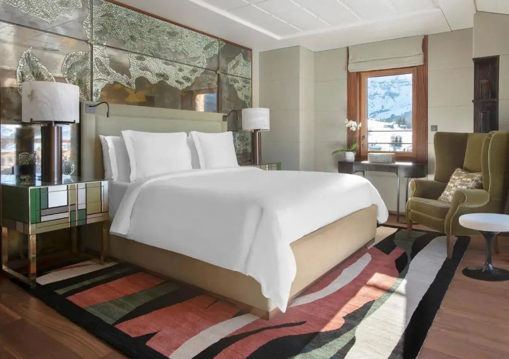 Moderne Suite mit großem Bett, künstlerischem Teppich und Aussicht auf verschneite Berge.