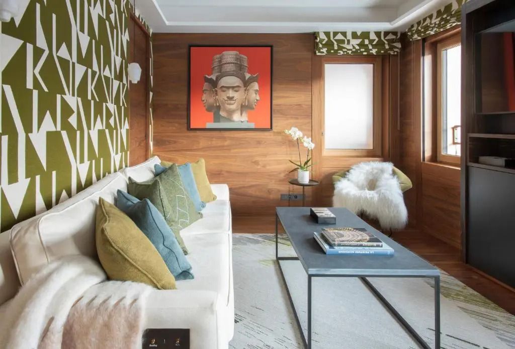 Gemütliches Wohnzimmer mit Designer-Sessel, Sofa, Kissen und kunstvollem Bild an der Wand.