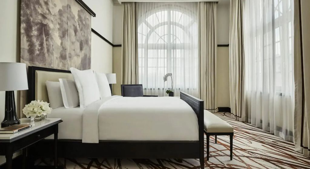 Elegantes Schlafzimmer mit großem Doppelbett und bodentiefen Fenstern mit Vorhängen.