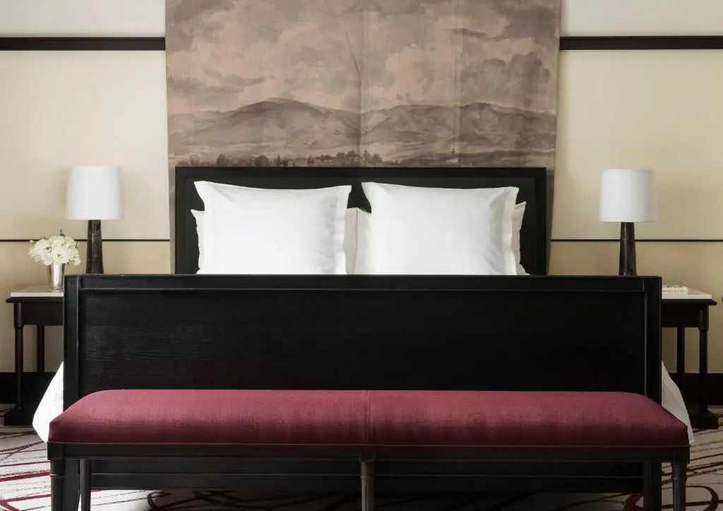 Doppelbett mit weißer Bettwäsche und kunstvollem Wandhintergrund.