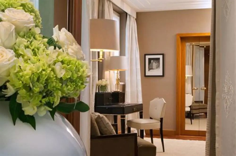 Helles Hotelzimmer mit Blumenarrangement, Schreibtisch und Stuhl neben einem großen Spiegel.