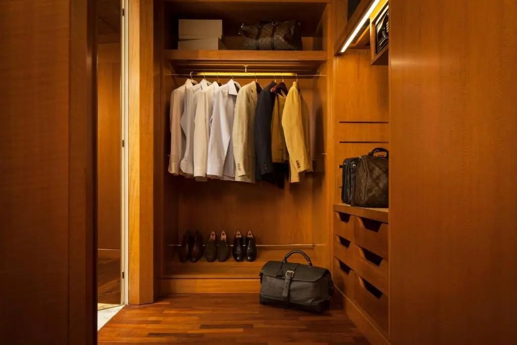 Ein geräumiger Holzkleiderschrank mit aufgehängten Kleidungsstücken und edlen Ledertaschen.