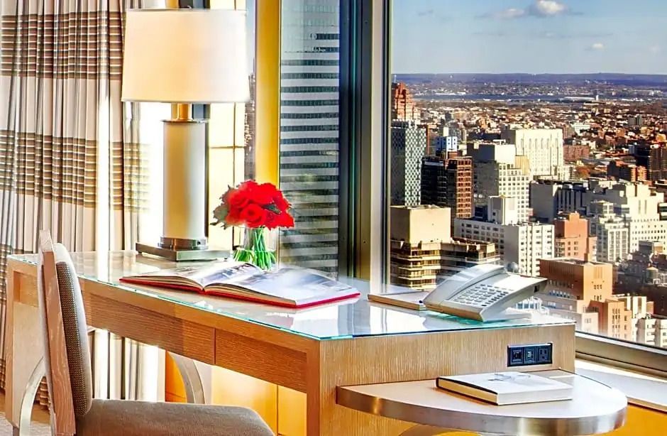 Schreibtisch mit Stadtblick und roten Rosen im Glas.