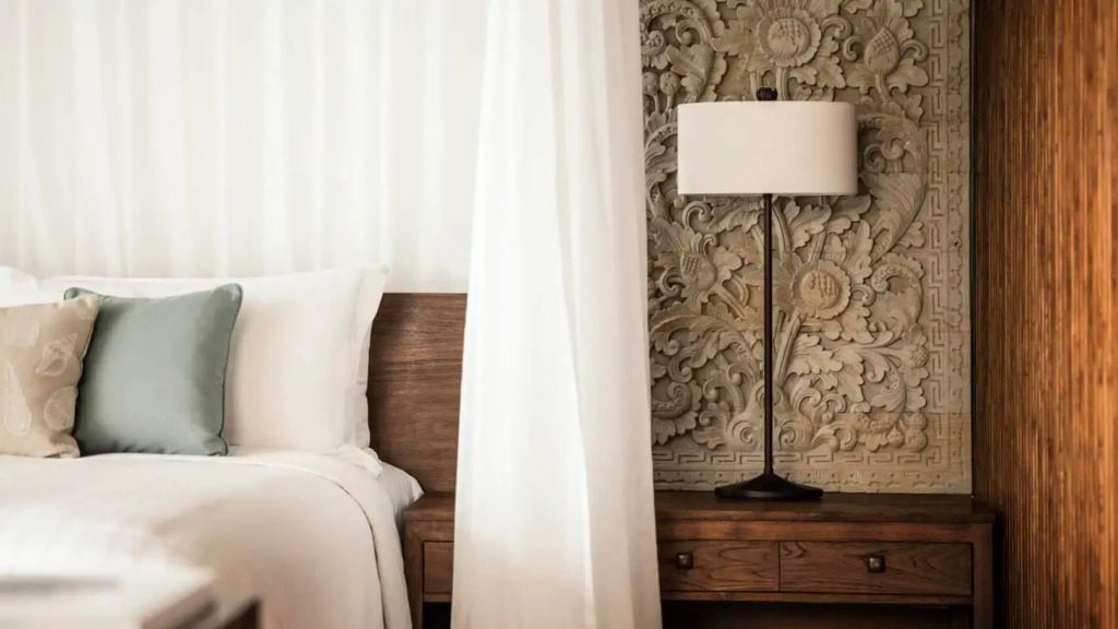 Detailreiches Wandrelief hinter einem Bett mit Beistelltisch und Lampe.