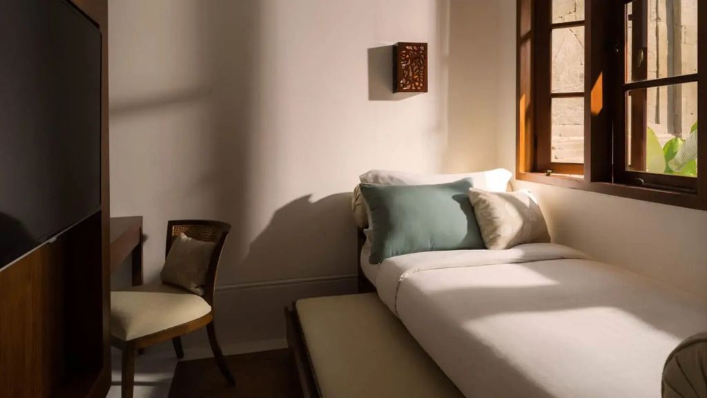 Sonnendurchflutetes Zimmer mit modernem Bett und Sitzgelegenheit.