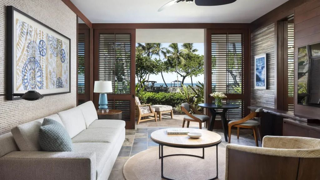 Wohnbereich mit Sofas und Tisch, Blick auf Garten und Meer durch große Fenster