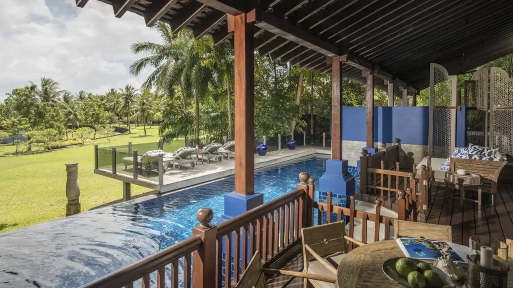 Privater Pool mit Liegestühlen in tropischer Gartenumgebung und überdachter Terrasse.
