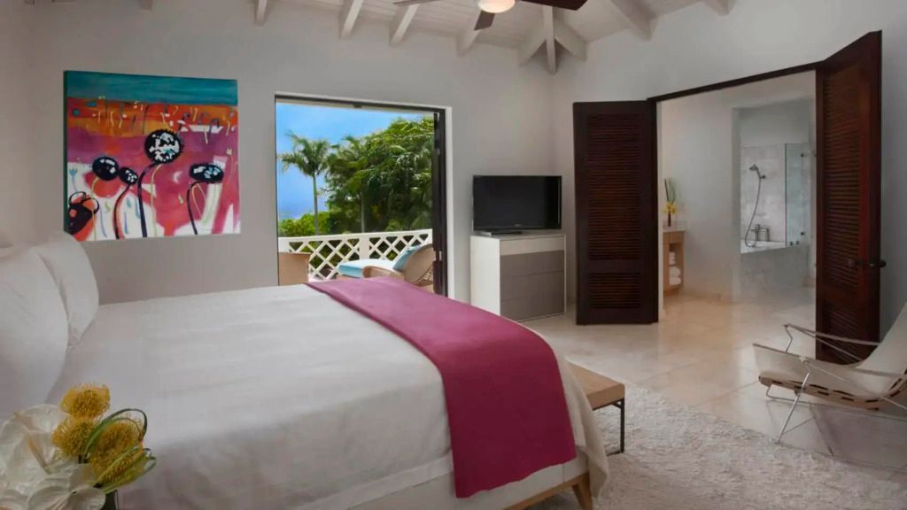 Helles Schlafzimmer mit Blick auf tropische Vegetation und Zugang zur Terrasse.