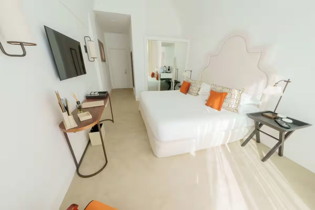 Helles Zimmer mit Doppelbett, großem Spiegel und Flachbildfernseher.