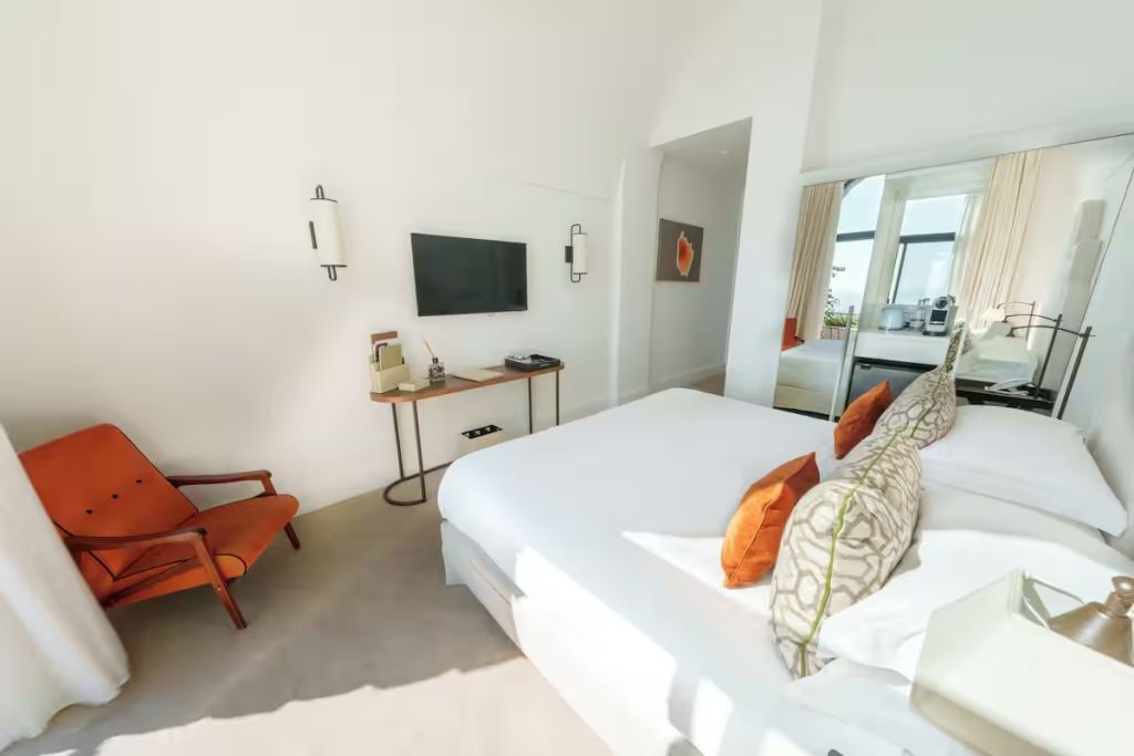Doppelzimmer mit stilvollen Kissen, Fernseher und gemütlichem Sessel.