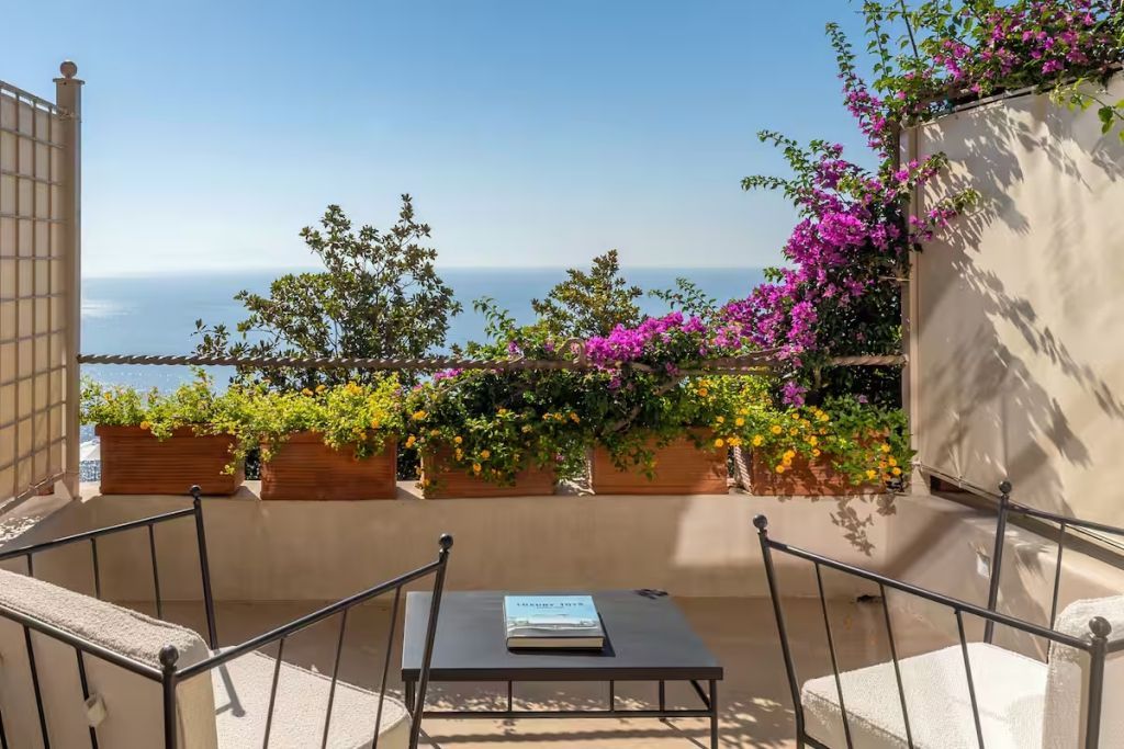 Terrasse mit Meerblick und blühenden Pflanzen. Sitzgelegenheiten vorhanden.