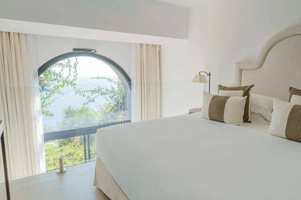 Helles Zimmer mit großem Bett und Blick auf das Meer durch ein rundes Fenster