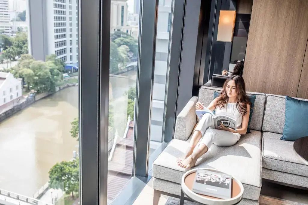 Person liest in moderner Suite mit Blick auf den Fluss durch bodentiefe Fenster