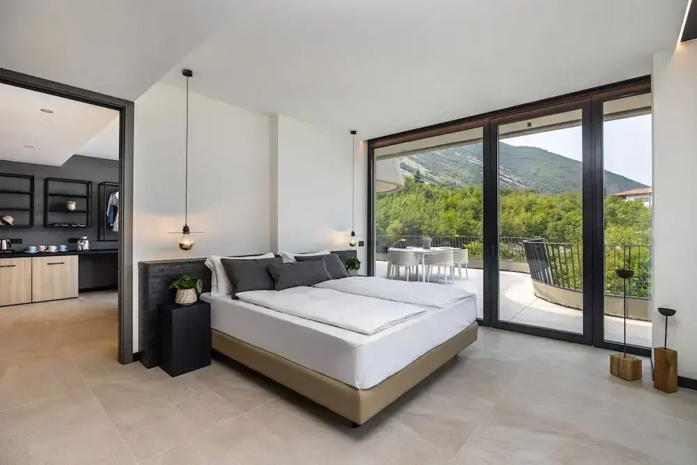 Helles Schlafzimmer mit Doppelbett und großem Fenster sowie Balkon mit Seeblick