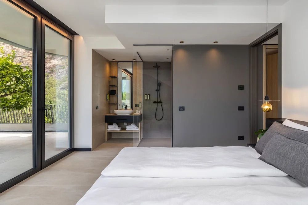 Schlafbereich und Badezimmer in moderner Suite mit Glasfront und Seeblick