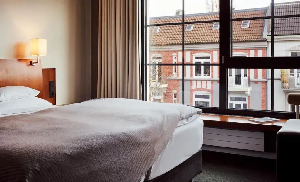 Gemütliches Doppelbett mit Stadtblick durch ein großes Fenster