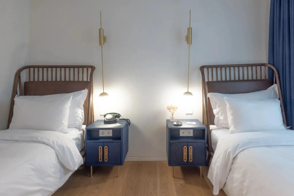 Zwei Einzelbetten mit blauen Nachttischen und eleganten Lampen im Darling Zimmer