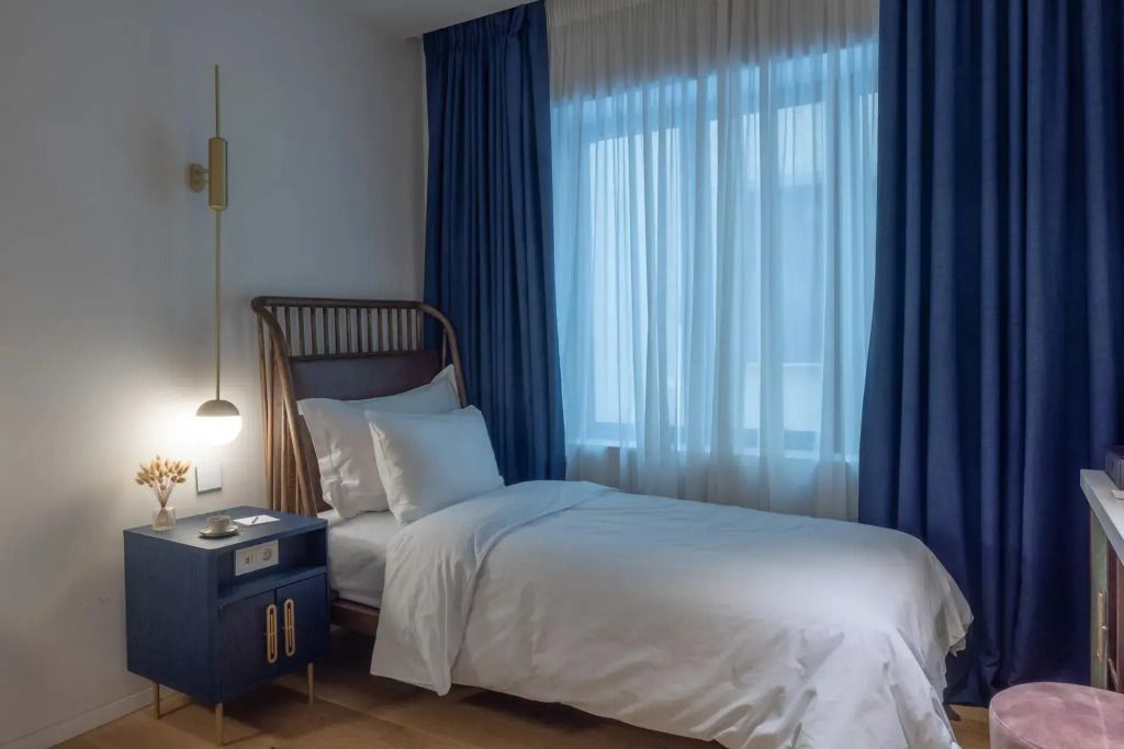 Gemütliches Einzelbett mit blauen Vorhängen und modernem Nachttisch