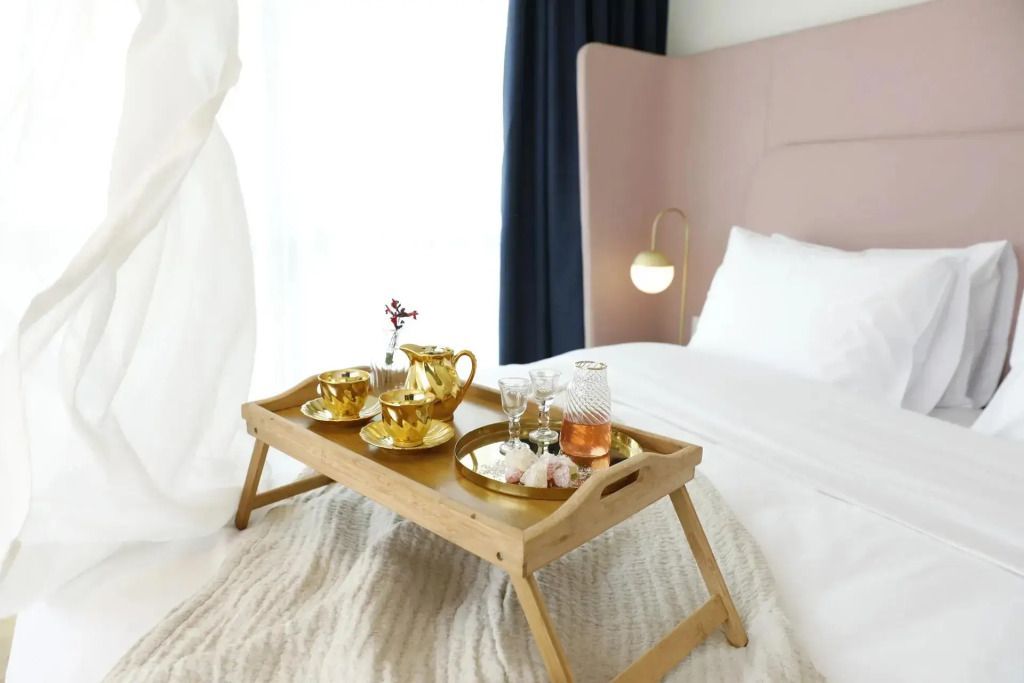 Frühstückstablett mit goldener Teekanne und Tassen auf Bett in Suite