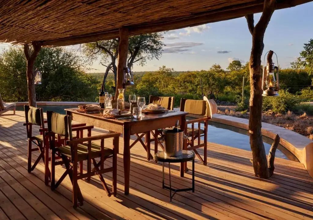 Deck mit Essbereich und Blick auf den Pool und die Savanne bei Sonnenuntergang.